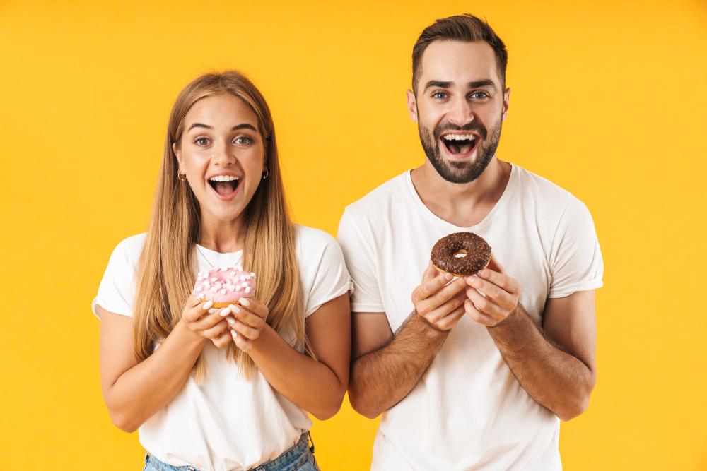 image-of-excited-couple-man-and-woman-smiling-while-holding-sweet-donuts-together-isolated-over-yellow-wall.jpg