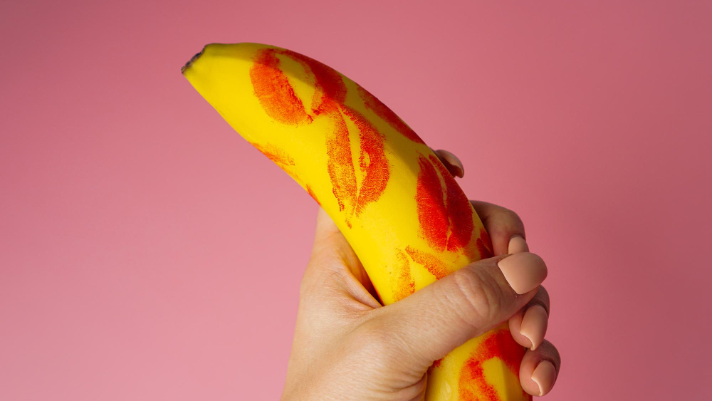 woman-hand-holding-banana-with-red-lipstick-markings-on-pink-background.jpg